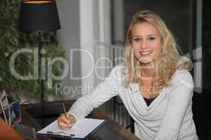 Young blond woman writing on clipboard