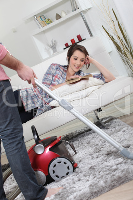 Husband vacuuming whilst wife lays on sofa