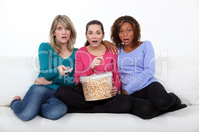 Three scared women sat on sofa watching movie