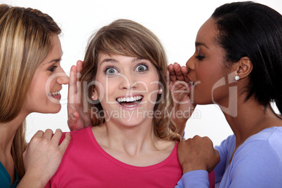 Two women whispering into friends ear