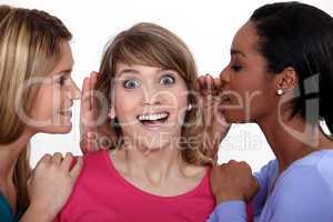Two women whispering into friends ear