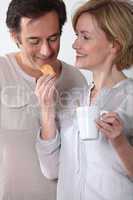 Woman with cup of coffee feeding her partner a biscuit