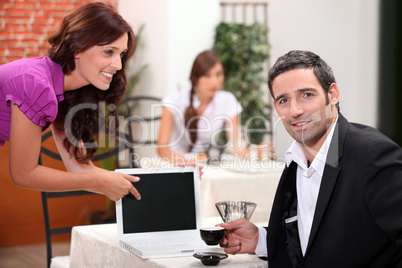 Woman in a restaurant pointing to a computer screen left blank for your image