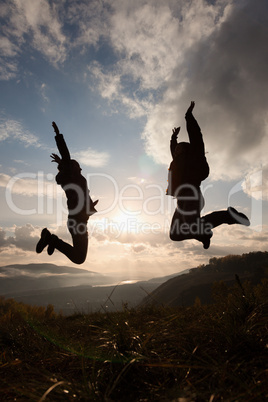 Happy young woman and man jumping at the sunset