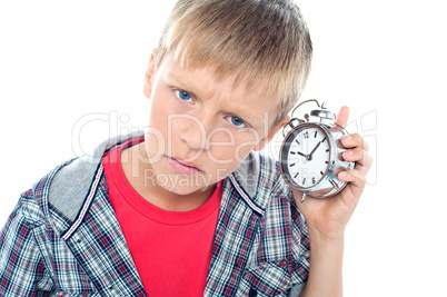 Confused young kid holding time piece close to his ear