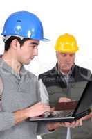young craftsman working on his laptop while senior craftsman is taking notes