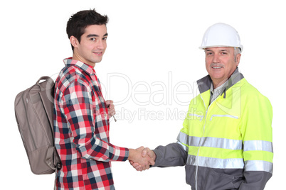young apprentice with backpack shaking hands with senior foreman