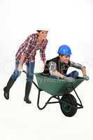 Two female construction workers racing in a wheelbarrow.