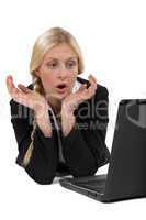 Shocked blond businesswoman sat in front of laptop