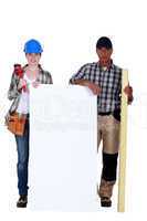 Plumber and carpenter stood by blank poster