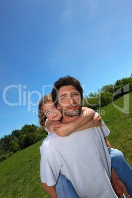 Man carrying little girl on his back in a meadow