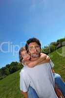 Man carrying little girl on his back in a meadow