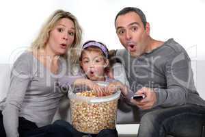 Parents with daughter watching TV and eating popcorn