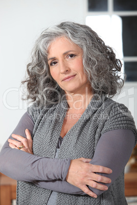 Grey haired woman stood in the kitchen with her arms folded