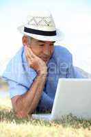 Elderly man laying in field with laptop