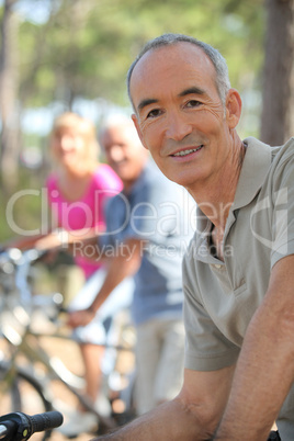 Older man riding a bike in the forest with friends