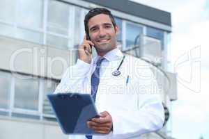 Male doctor outside hospital making phone call