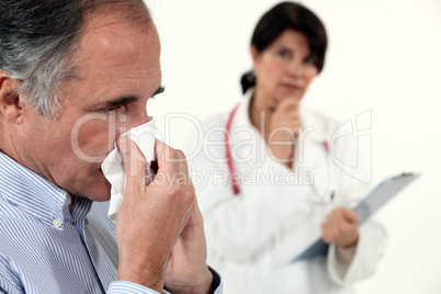 Man blowing his nose next to a doctor