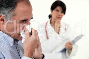 Man blowing his nose next to a doctor