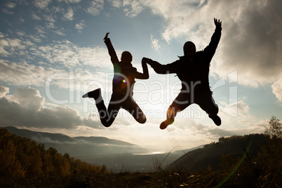 Happy young woman and man jumping at the sunset