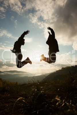 Happy young woman and man jumping at the sunset