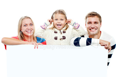 Young beautiful family behind white blank ad board