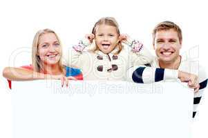Young beautiful family behind white blank ad board