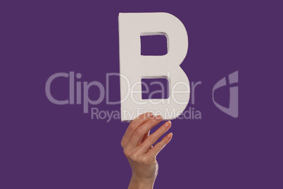 Female hand holding up the letter B from the bottom