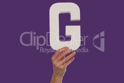 Female hand holding up the letter G from the bottom