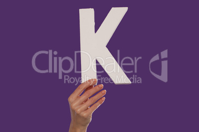 Female hand holding up the letter K from the bottom