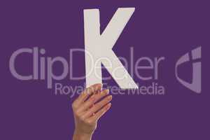 Female hand holding up the letter K from the bottom