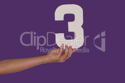 Female hand holding up the number 3 from the left