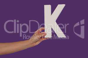 Female hand holding up the letter K from the left