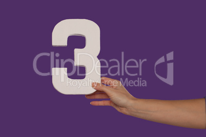 Female hand holding up the number 3 from the right