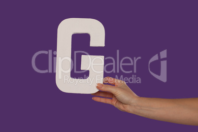 Female hand holding up the letter G from the right