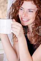 Junge hübsche Frau mit Sommersprossen trinkt eine Tasse Kaffee