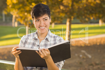 Mixed Race Young Female Holding Open Book and Pencil Outdoors