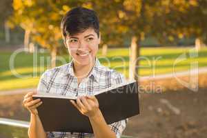 Mixed Race Young Female Holding Open Book and Pencil Outdoors