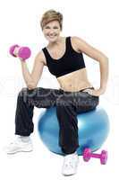 Woman seated on fitness ball doing dumbbells