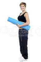 Smiling female instructor carrying a blue yoga mat