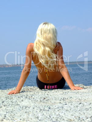 The girl-blonde sits on coast of a gulf