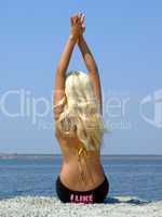 The girl-blonde sits on coast of a gulf, having lifted hands upw