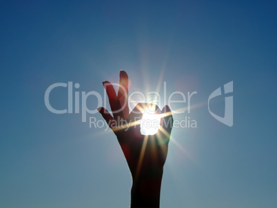 Silhouette of a female hand, the blue sky and the bright sun