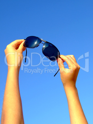 Female hands hold sunglasses on a background of the blue sky