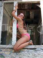 The sexual girl in bikini sits in a window of the destroyed hous