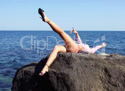 The sexual girl lays on a stone on a background of the sea
