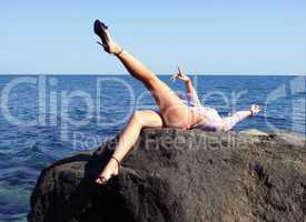 The sexual girl lays on a stone on a background of the sea