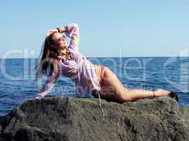 The sexual girl lays on a rock and looks at the sun