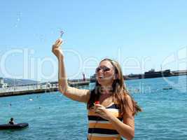 The beautiful girl starts up soap bubbles on quay