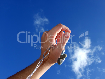 Hand with small headphones on a background of the blue sky